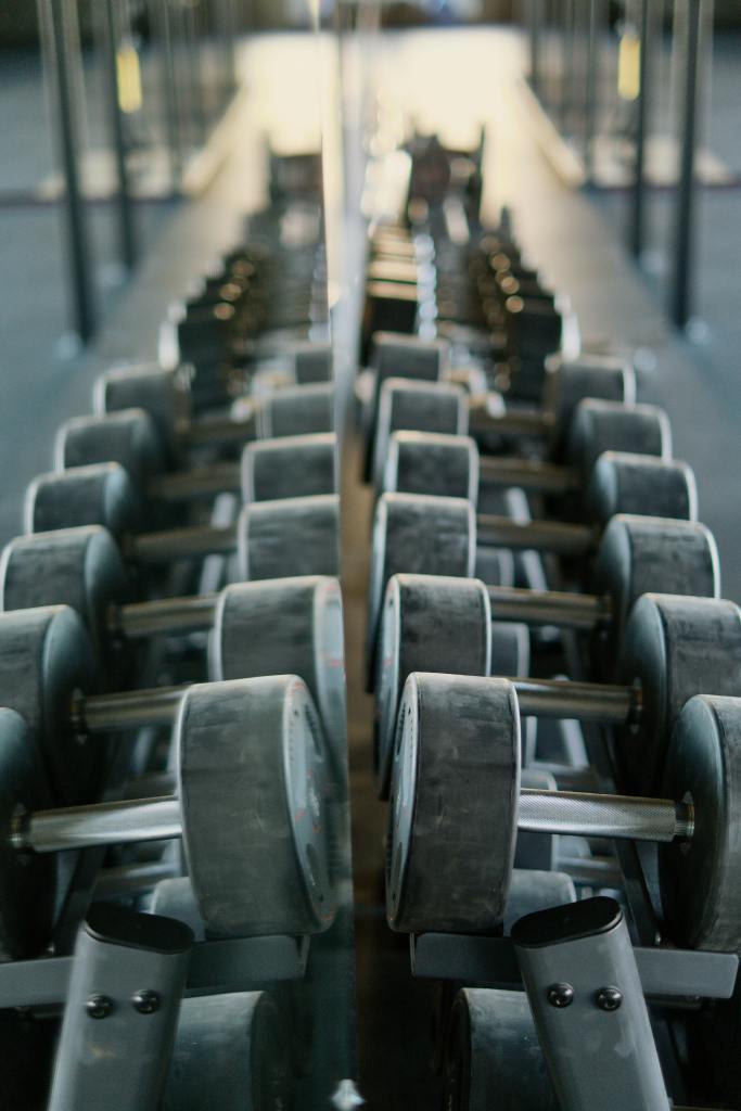 Rows of dumbbells neatly arranged in a gym with a mirrored background.